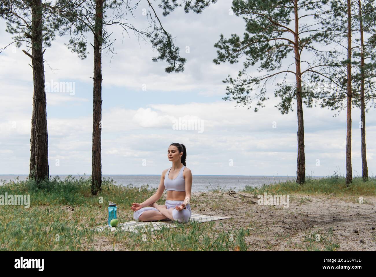 Brünette junge Frau in Sportkleidung sitzt in Lotuspose und meditiert auf Yoga-Matte Stockfoto