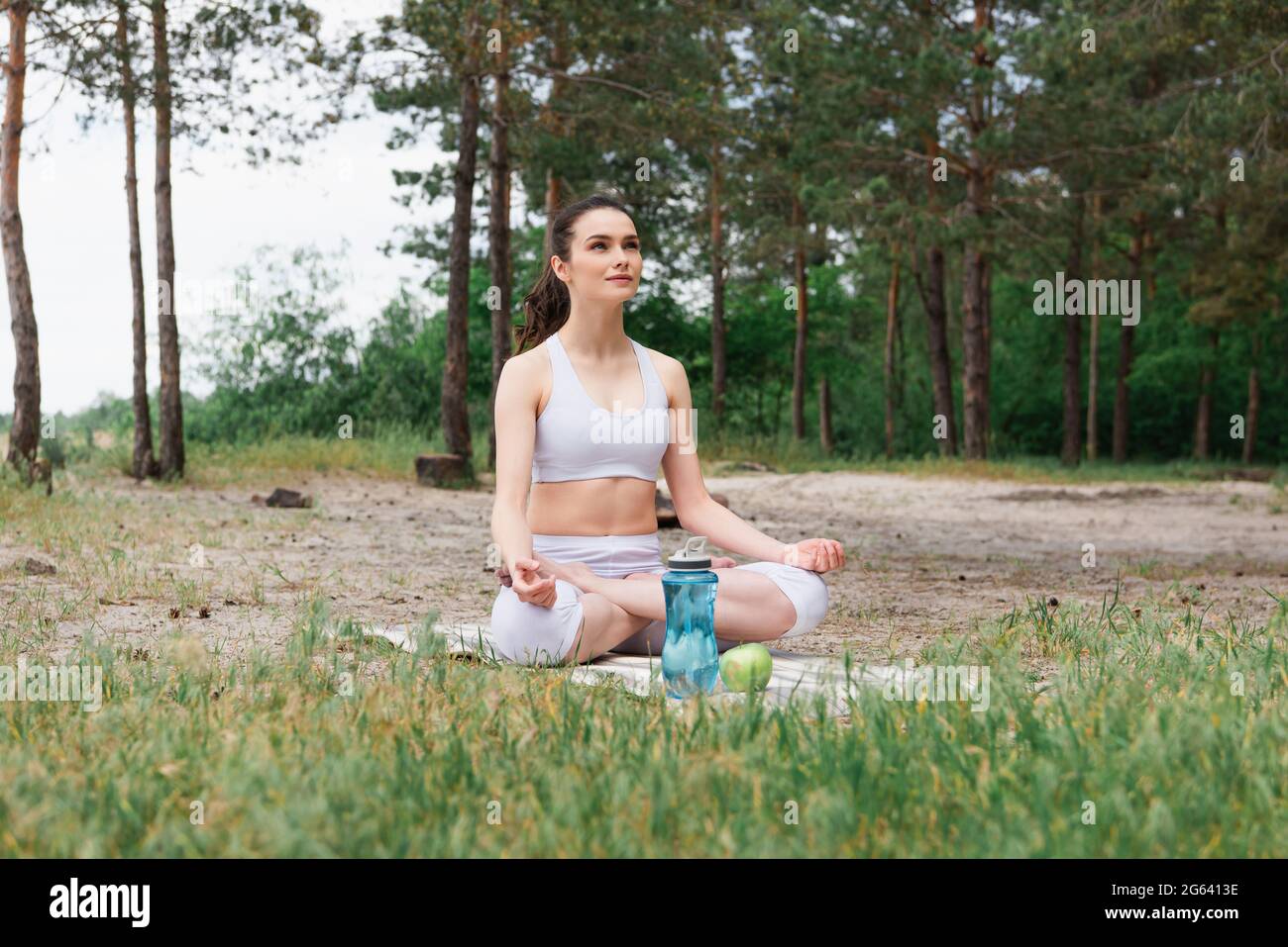 Junge Frau in Sportkleidung sitzt in Lotushaltung und meditiert auf einer Yogamatte Stockfoto