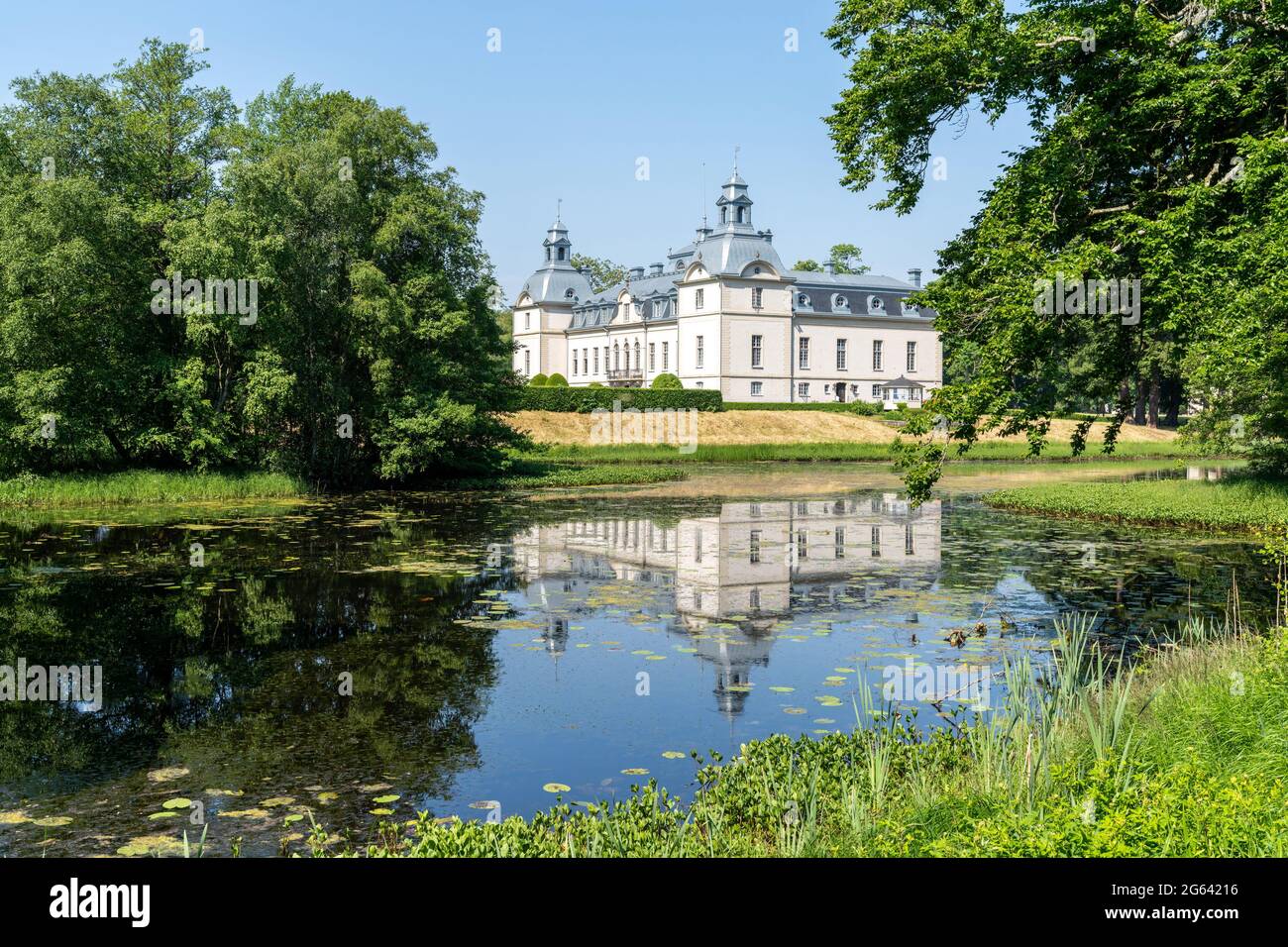 Tomelilla, Schweden - 19. Juni 2021: Das malerische Schloss Kronovall und seine Gärten spiegeln sich an einem Sommertag unter blauem Himmel in einem Teich im Vordergrund wider Stockfoto