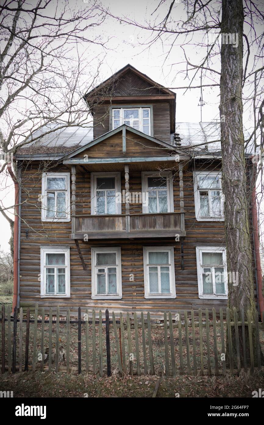 Altes Holzhaus mit Dachboden und weißen Rahmen hinter einem Zaun zwischen Ästen Stockfoto