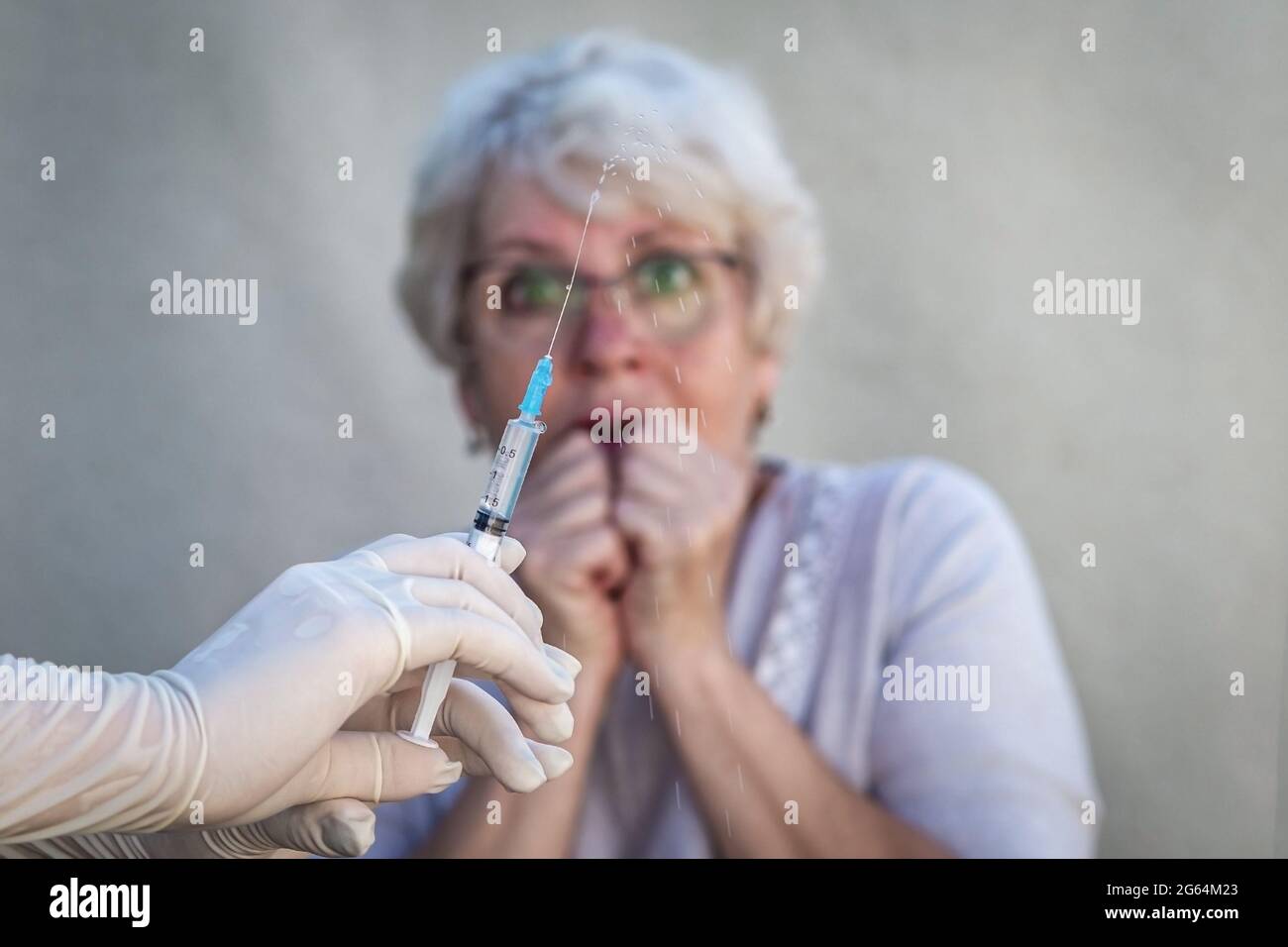 Hände in medizinischen Handschuhen halten eine Spritze, bereiten sich auf die Impfung vor, im Hintergrund hat eine ältere Frau in einer Brille Angst, eine Injektion zu geben Stockfoto