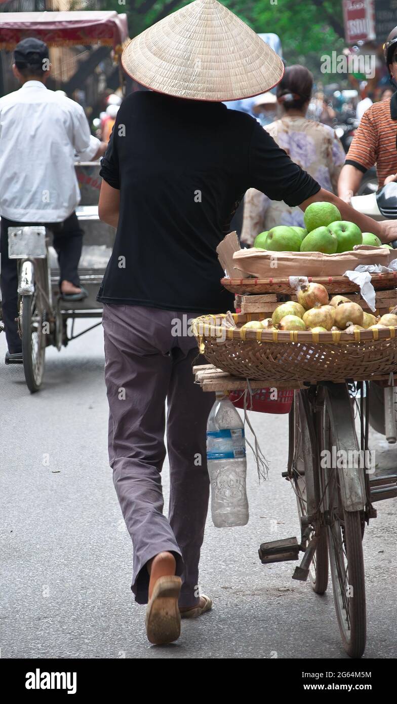 Eine Person, die einen Strohhut trägt, geht mit einem Fahrrad durch die  Straßen von Hanoi, Vietnam, mit Körben mit Äpfeln auf der Rückseite des  Fahrrads Stockfotografie - Alamy