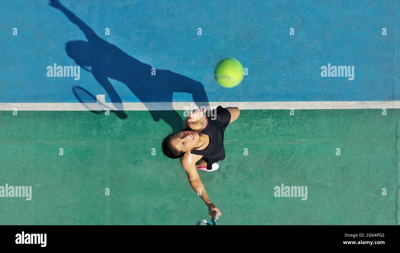 Aus der Perspektive einer jungen erwachsenen Tennisspielerin, die den Ball in die Luft wirft, um einen Schatten auf den Platz zu werfen. Stockfoto