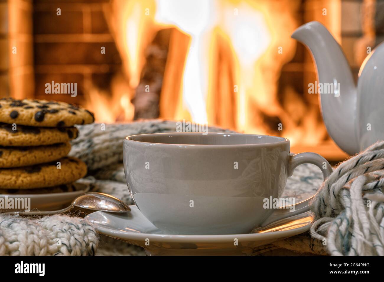 Gemütliche Kamin-Szene mit einer Tasse Kaffee Tee und Kekse auf einem Tisch, Reflexion von einem Feuer auf einem Glastisch. Stockfoto