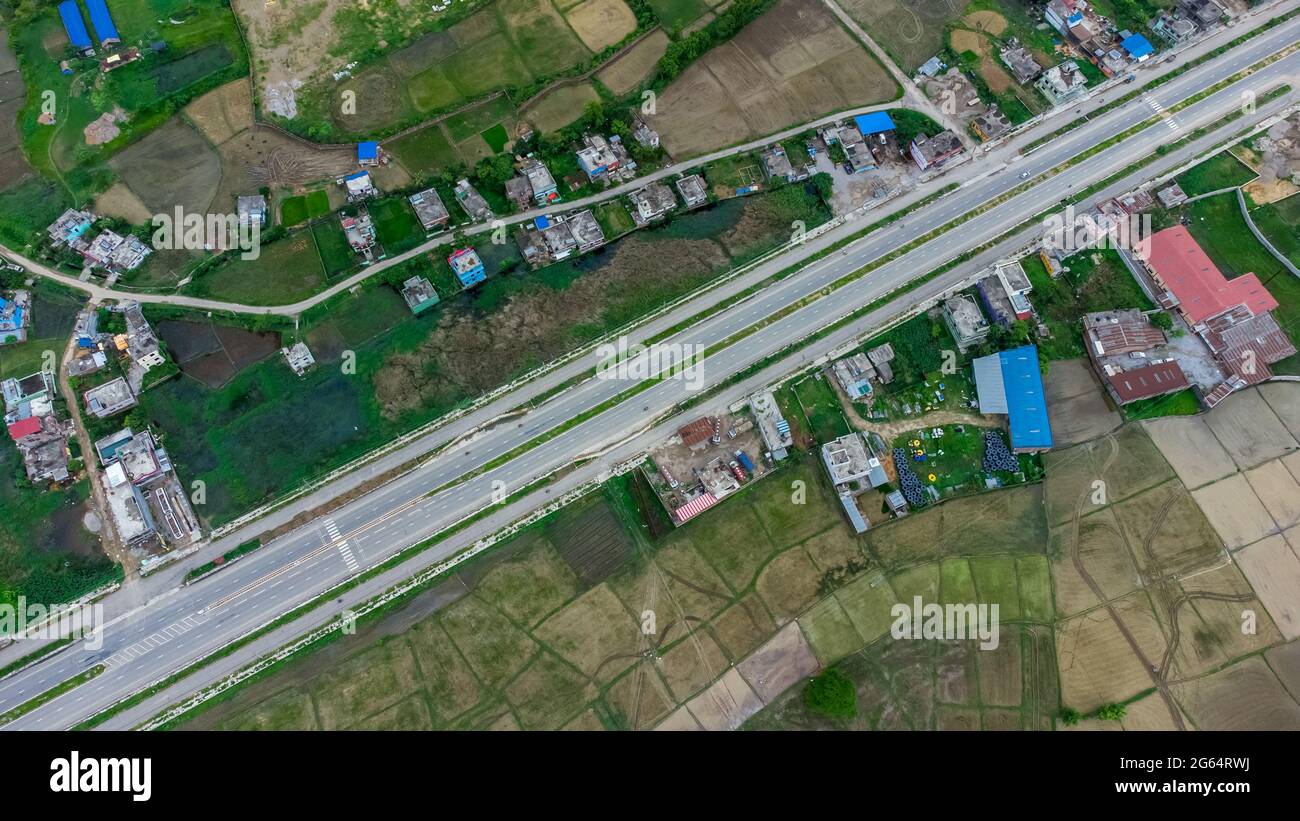 Luftaufnahme der sechsspurigen Autobahn, die durch Wiesen, Felder und verstreute Häuser in Richtung Berge im ländlichen Nepal führt. Stockfoto