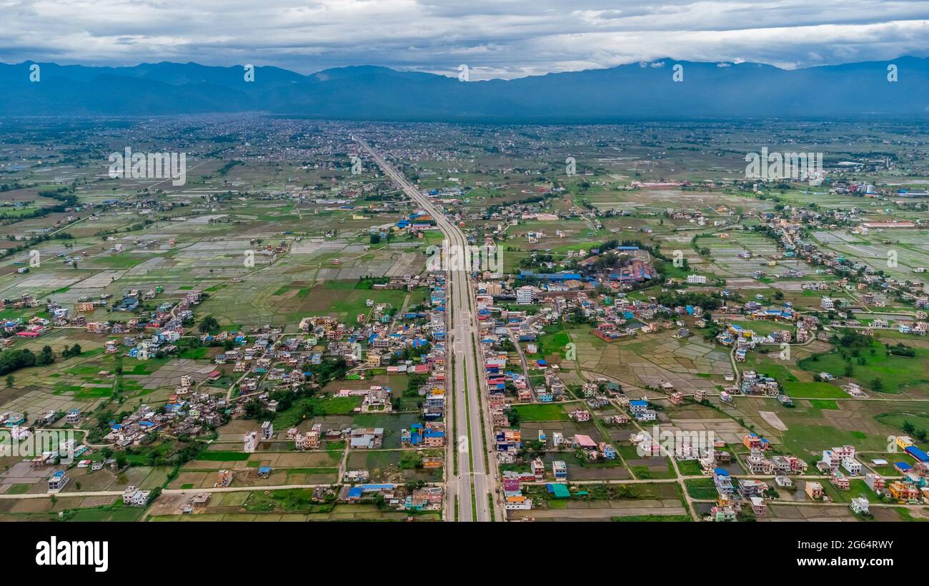 Luftaufnahme der sechsspurigen Autobahn, die durch Wiesen, Felder und verstreute Häuser in Richtung Berge im ländlichen Nepal führt. Stockfoto