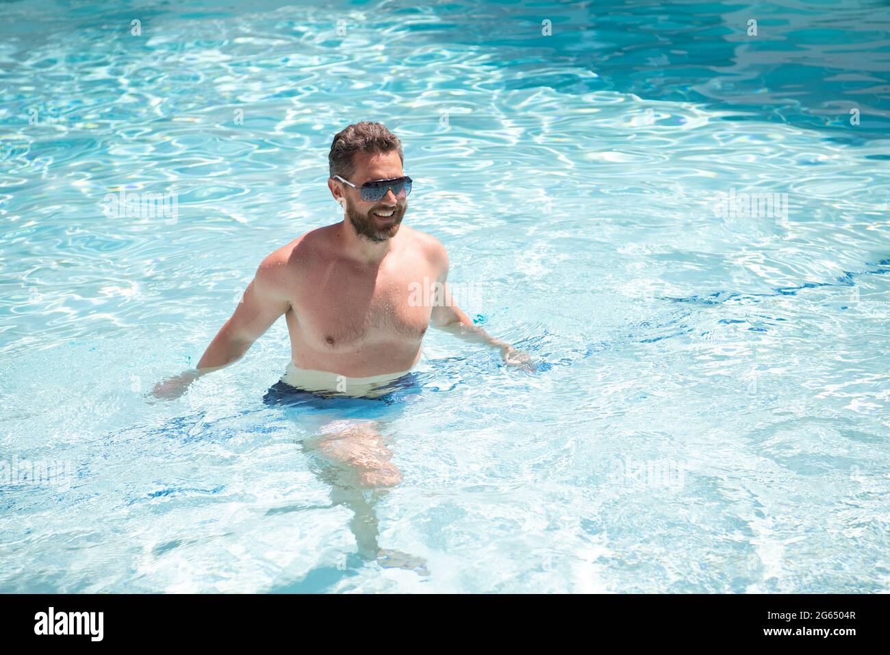 Glücklicher bärtiger Mann in Sonnenbrillen, der im Sommerurlaub im Wasser des Pools schwimmt Stockfoto