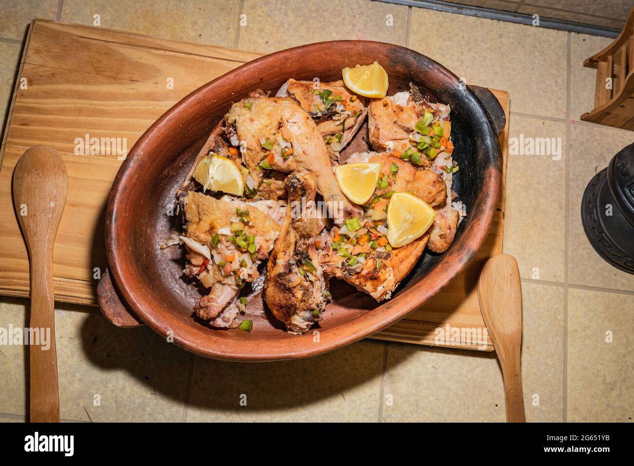 Hausgemachtes gegrilltes Hähnchen mit in Stücke geschnittenen Gewürzen in roter Keramik-Backform auf Holzbrett. Stockfoto