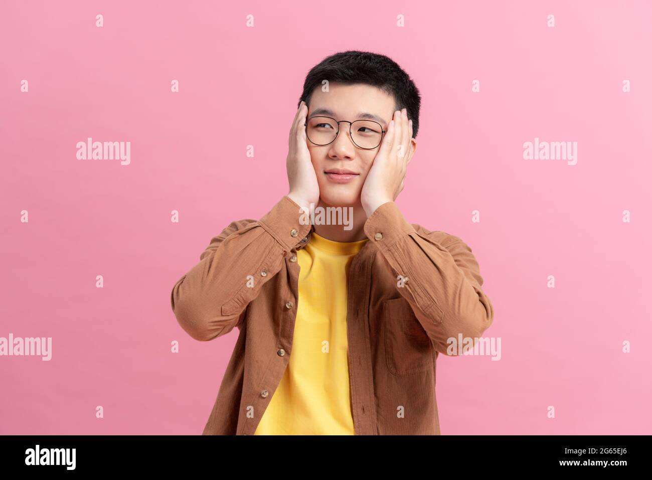 Beschämender lächelnder Mann, der sein Gesicht mit Händen bedeckt, die auf einem rosa Hintergrund isoliert sind Stockfoto