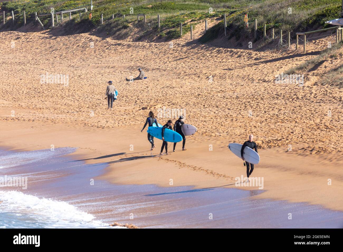 Australische Surfer tragen ihre Surfbretter am Avalon Beach in Sydney an einem sonnigen Wintertag, NSW, Australien Stockfoto