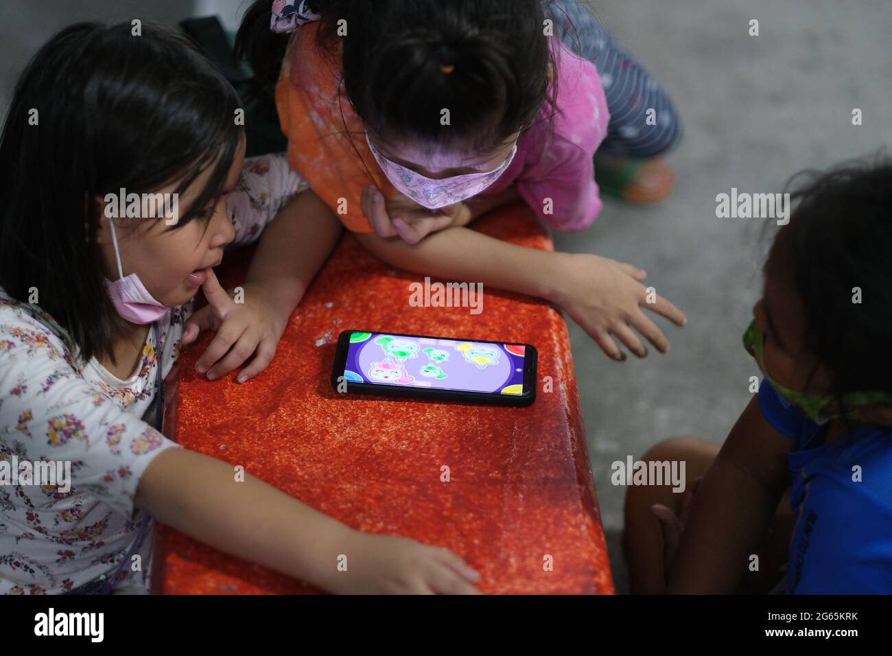 Drei thailändische Kinder spielen zusammen ein Logikspiel auf einem Smartphone Stockfoto