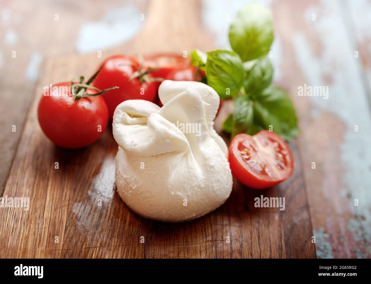 Burrata-Käse auf Holzbrett. Weicher Käse mit Tomaten und Basilikumblättern auf Holztisch. Leckere Burrata mit halber Tomate. Stockfoto