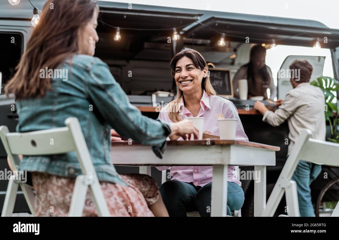 Glückliche reife Frauen, die Spaß beim Essen in einem Straßennahrungs-LKW im Freien haben Stockfoto