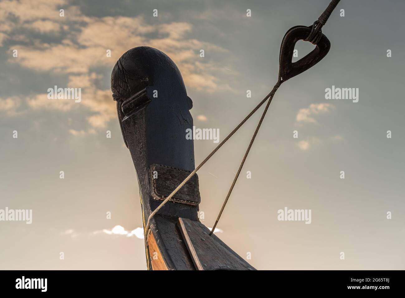 Bug eines Wikingerschiffes mit Segelseil vor Anker und Sonnenaufgangswolken im Hintergrund Stockfoto