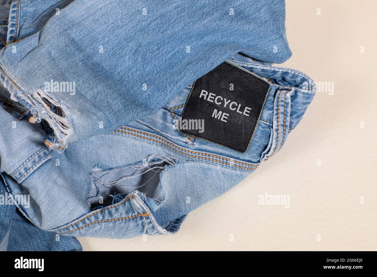 Recyceln Sie mich, blaue Jeans mit einem Kleidungsanhänger. Kreislaufwirtschaftsprinzip, Zero Waste Konzept. Wiederverwendung von Materialien und Reduzierung von Abfall in der Mode. Denim-TRO Stockfoto