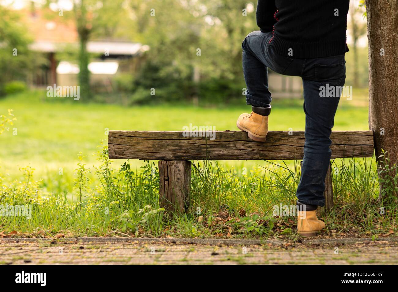 Arbeiter oder Landwirt in legerer Kleidung, der seinen Fuß auf einer rustikalen Bank ausruht, während er über ein grünes grasfeld blickt und sich entspannt, die Natur genießt Stockfoto