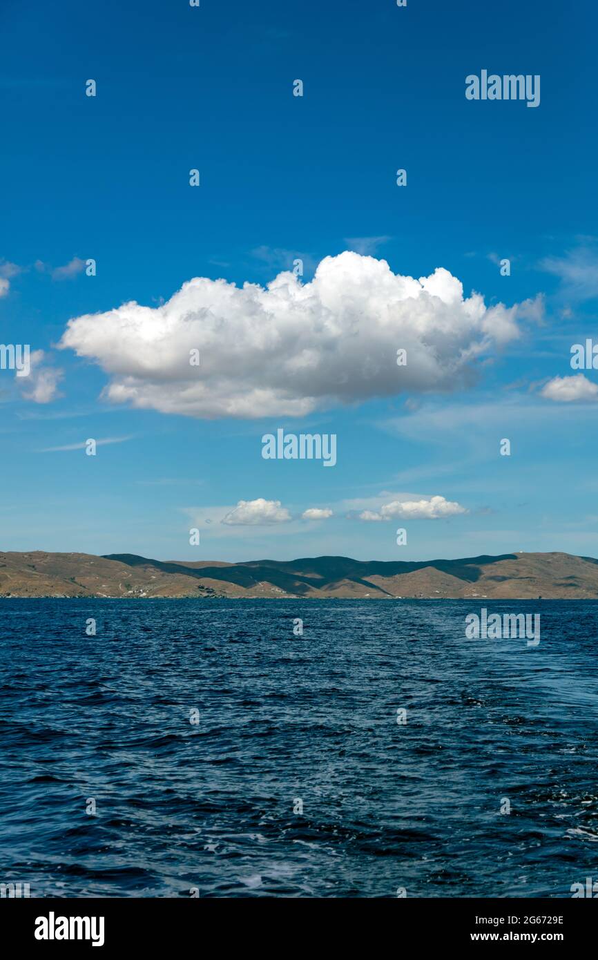 Wolke flauschig und Cumulus auf klaren blauen Himmel, über einer griechischen Insel, Kykladen, Griechenland. Sonniger Frühlingstag. Felsiges Land, gewelltes Meer, Wolkenschatten auf den coas Stockfoto