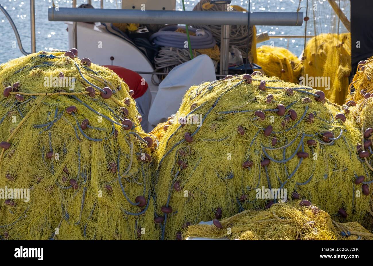 Fangnetze stapeln sich in einem Trawler. Gelbe Farbe Netze mit Seilen und schwimmt trocknend unter der Sonne, glänzend gewellten Meeresgrund. Griechische Insel Kyklade Stockfoto