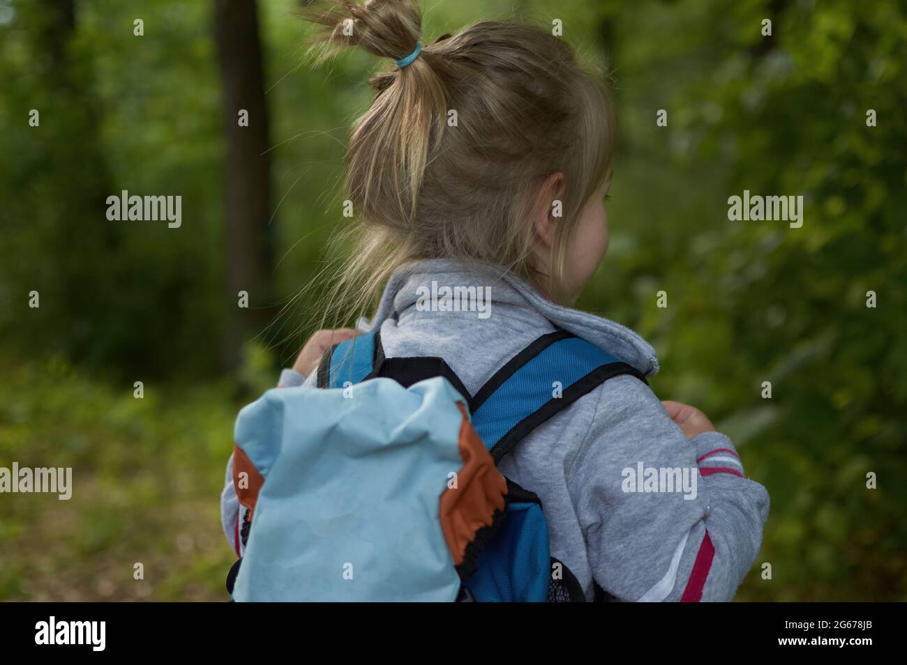 Ein glückliches kleines Mädchen mit einem Rucksack, das in einem Waldpark im Frühling wegschaut Stockfoto