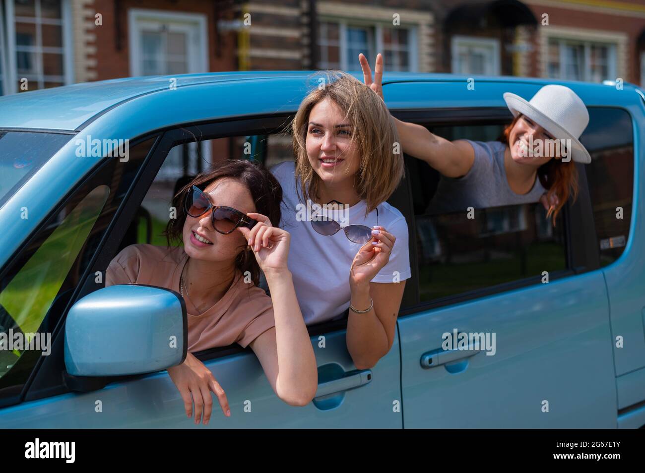 Drei fröhliche kaukasische Freundinnen schauen aus dem Autofenster. Aufgeregt Frauen gehen auf einen Roadtrip. Die Brünette Blondine und der Rotschopf gehen weiter Stockfoto