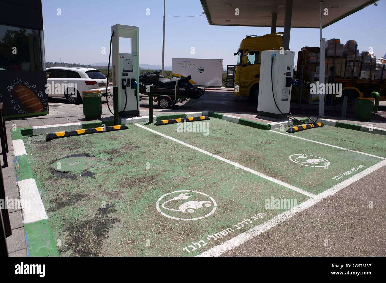 Zwei Ladestationen für Elektroautos mit ausgewiesenen grünen Parkplätzen, die auf Hebräisch für Elektroautos gekennzeichnet sind, nur an einer normalen Gas- oder Tankstelle. Stockfoto