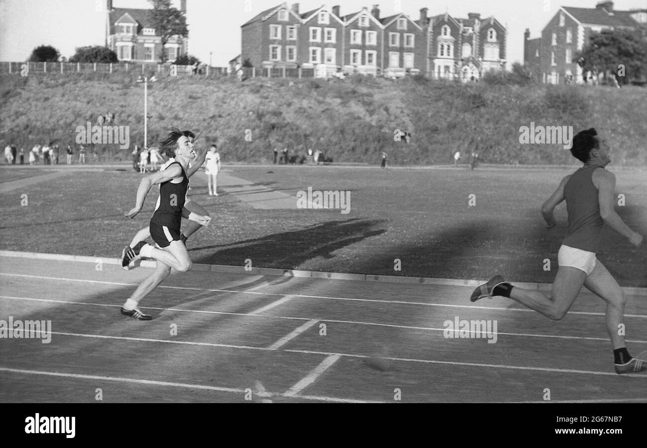 1960s, historisch, Leichtathletik, draußen auf einer Schlackenbahn, drei junge Männer, die an einem Laufrennen an einem Sporttag zwischen den Grafschaften, England, Großbritannien, teilnehmen. Stockfoto