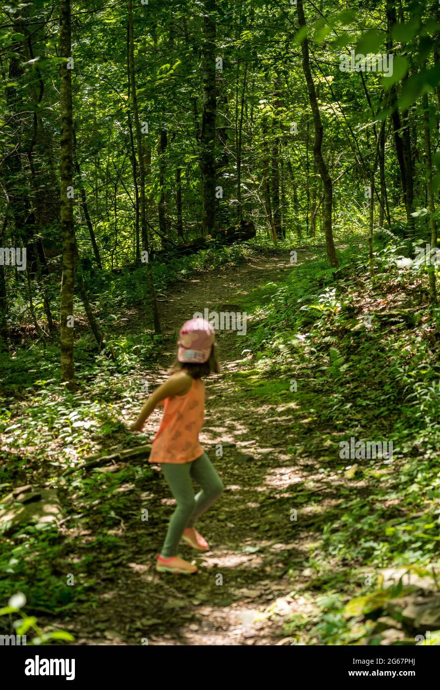 Kleines kaukasisches Mädchen, das Angst hat, dass jemand ihr in einem Wald folgt und auf dem Weg auf ihren Stalker zurückblickt Stockfoto