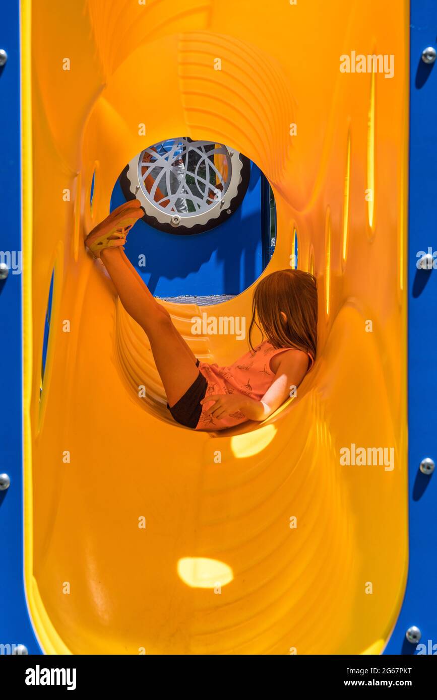 Junges Mädchen in Seitenansicht entspannen in einem gelben Plastikrohr oder Rohr auf Spielplatz Klettergerüst und Rutsche Stockfoto