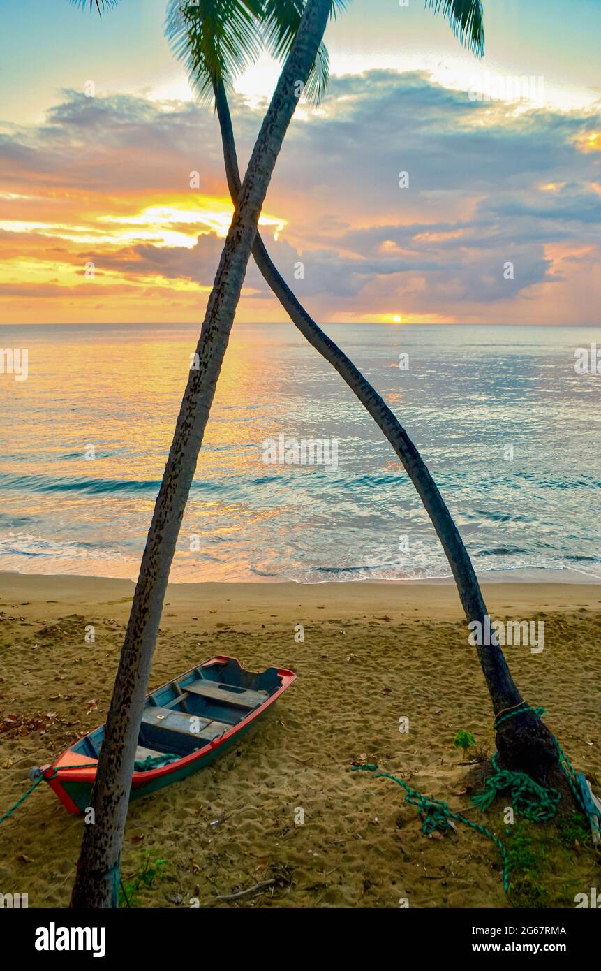 Sonnenuntergang an einem Puerto-ricanischen Strand mit Palmen und traditionellem Fischerboot. Rincon, PR. Stockfoto