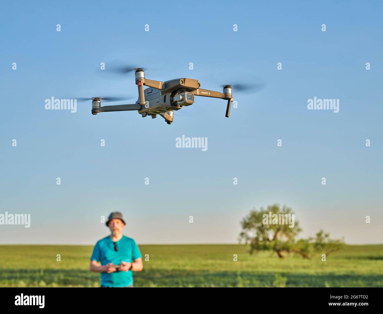 Briggsdale, CO, USA - 8. Juni 2021: Funkgesteuerte DJI Mavic 2 Pro Quadcopter Drohne fliegt über grüne Prärie mit einem männlichen Piloten im Hintergrund. Stockfoto