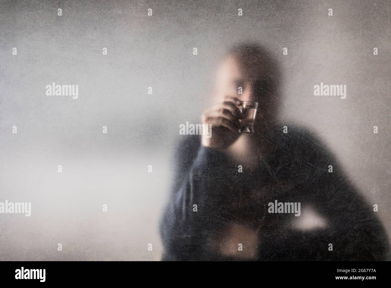 Mann mit einem Glas Wodka hinter einem staubigen zerkratzten Glas. Alkoholismus-Konzept. Stockfoto