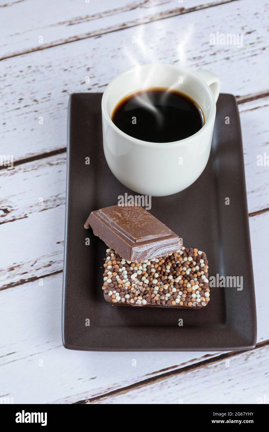 Milchschokoladenriegel mit Streuseln neben einer Tasse Kaffee (vertikales Foto). Stockfoto