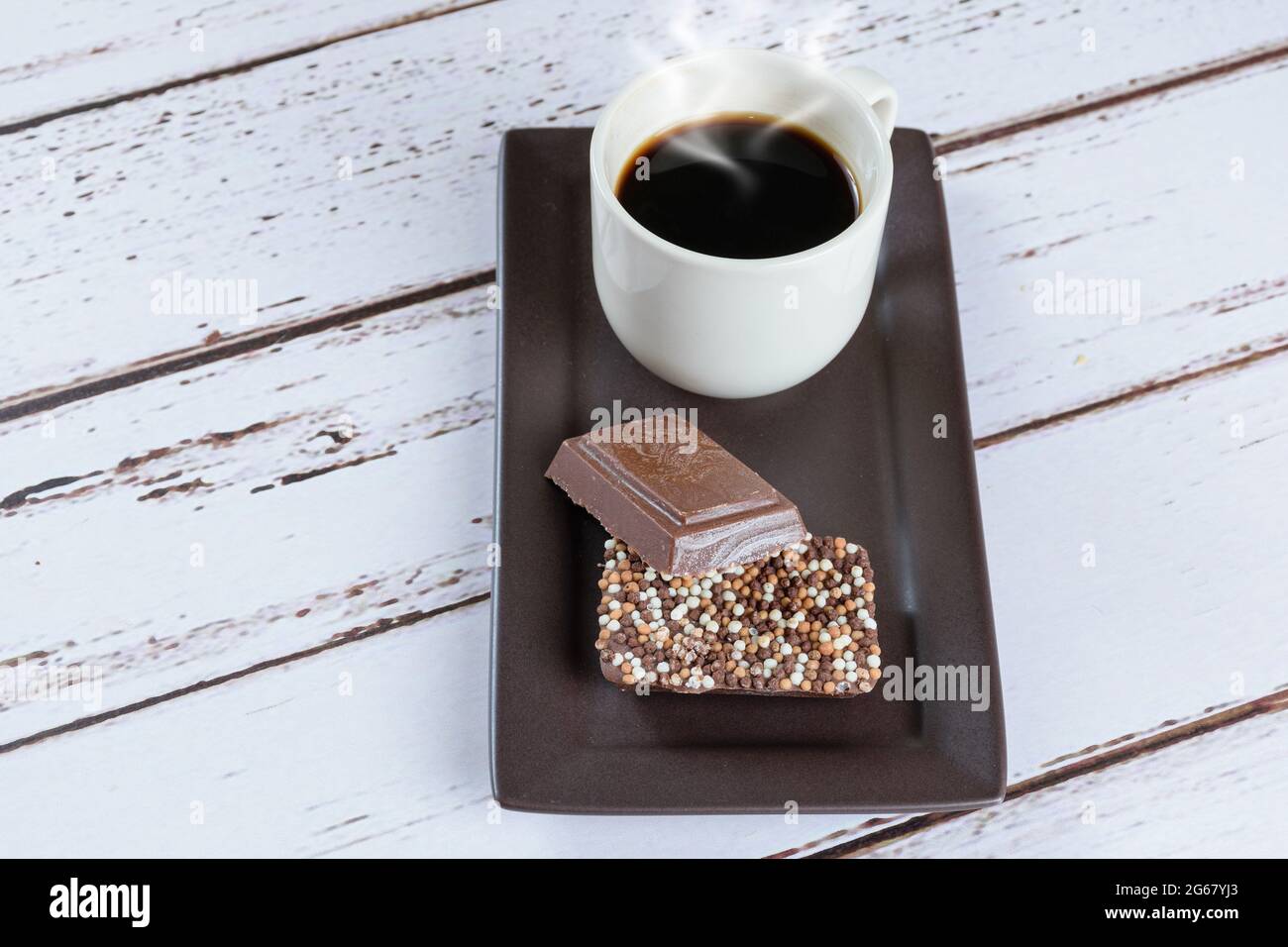 Milchschokoladenriegel mit Streuseln neben einer Tasse Kaffee. Stockfoto