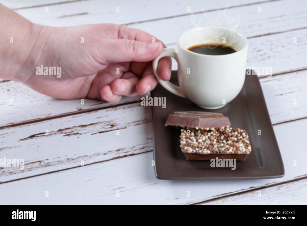 Milchschokoladenstangen mit Streuseln. Im Hintergrund eine Frau, die eine Tasse Kaffee bekommt. Stockfoto