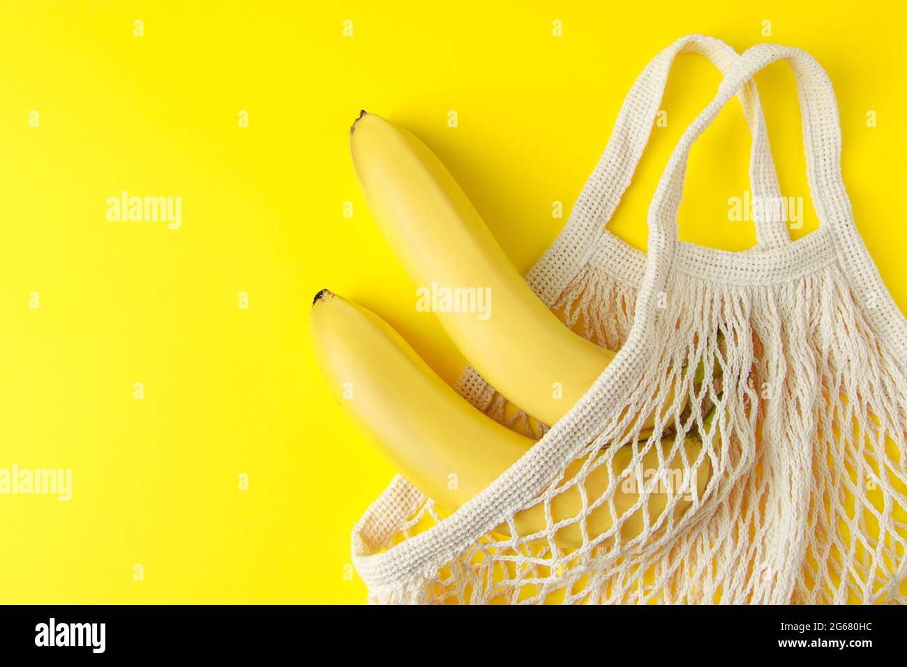 Reife Bananen in einem Netzbeutel auf gelbem Hintergrund. Umweltfreundliche Einkaufstasche aus Baumwolle. Bio-Früchte. Nachhaltiger Lebensstil und recycelbarer Abfall concep Stockfoto
