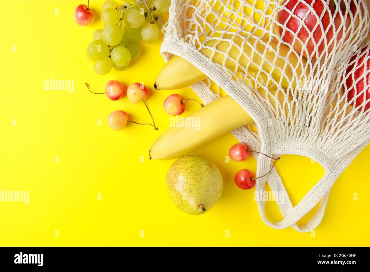 Umweltfreundliche Einkaufstasche aus Baumwolle. Reife Früchte in einem Netzbeutel auf gelbem Hintergrund. Vegane Bio-Lebensmittel. Nachhaltiger Lebensstil und Zero Waste Konzept. Stockfoto