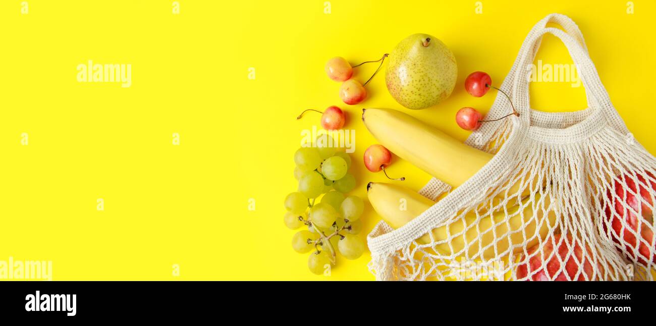 Reife Früchte in einem Netzbeutel auf gelbem Hintergrund. Umweltfreundliche Tasche aus Baumwollstring zum Einkaufen. Vegane Bio-Lebensmittel. Bannerformat. Stockfoto