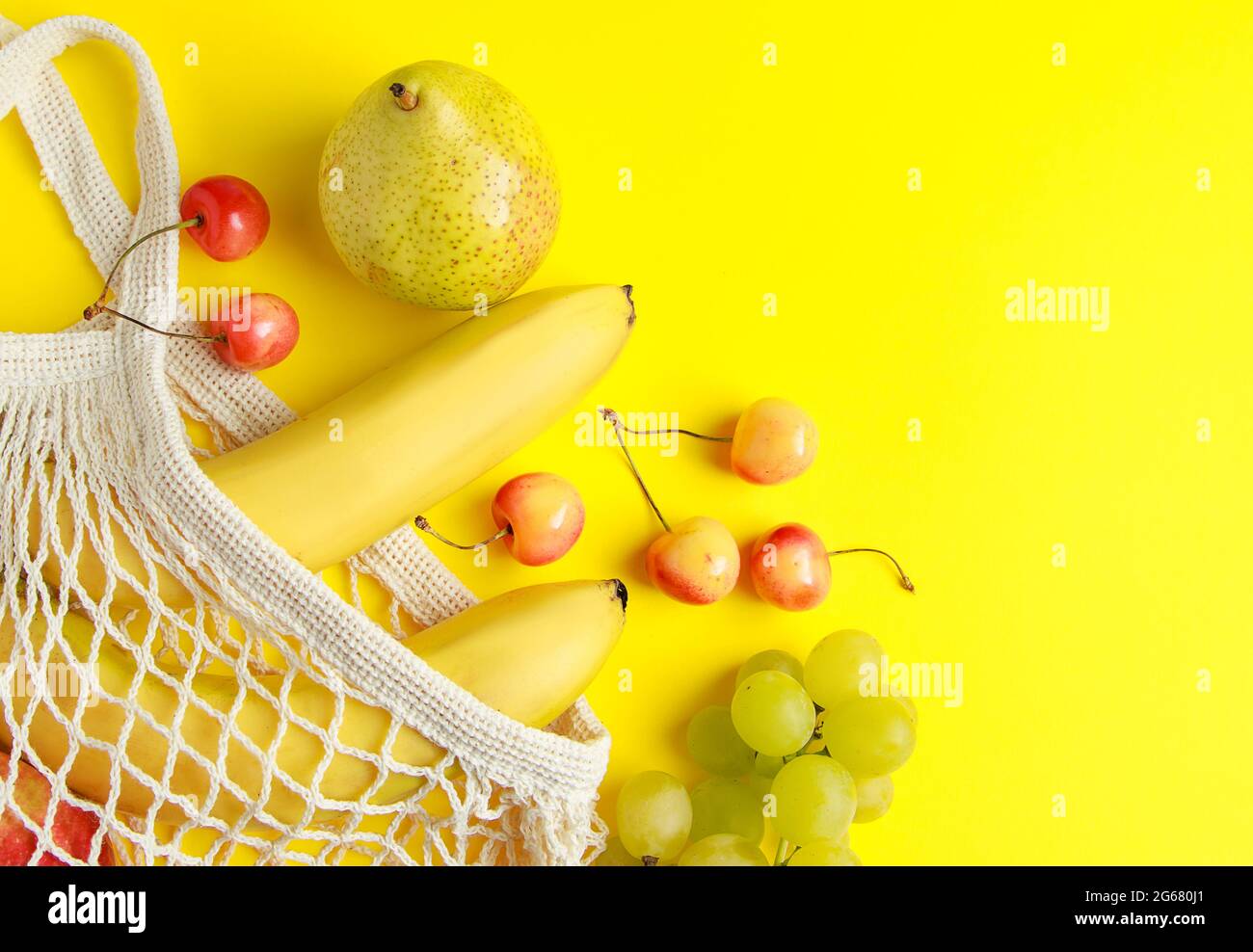 Umweltfreundliche Einkaufstasche aus Baumwolle. Reife Früchte in einem Netzbeutel auf gelbem Hintergrund. Vegane Bio-Lebensmittel. Nachhaltiger Lebensstil und Zero Waste Konzept. Stockfoto