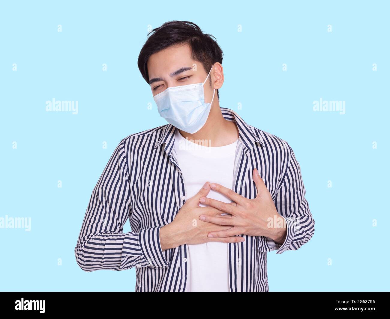 Der junge Mann trägt eine medizinische Schutzmaske, fühlt sich mit den Händen auf der Brust unbehaglich, hat Schwierigkeiten beim Atmen. Stockfoto