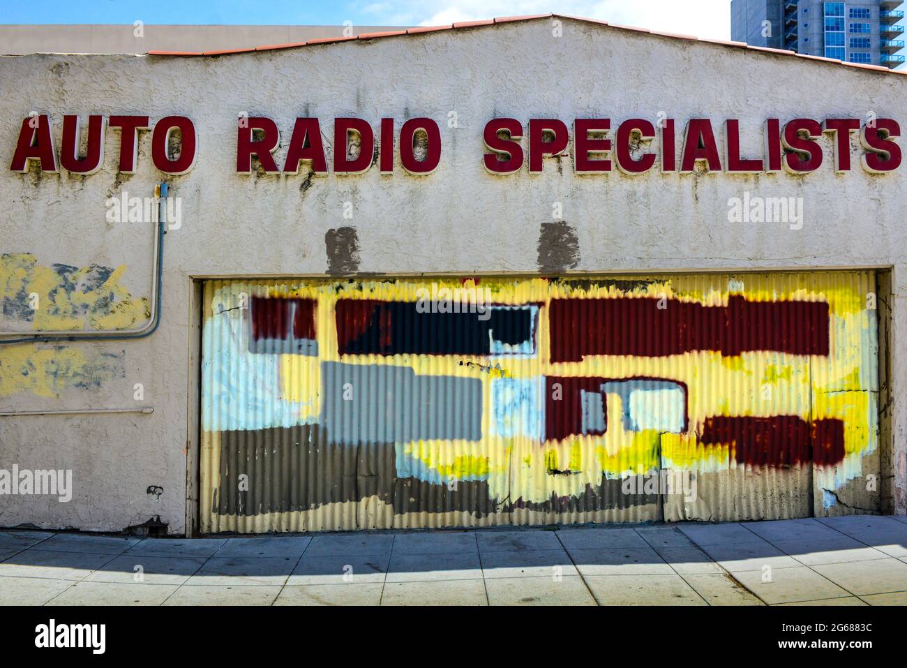 Ein verlassenes Industriegebäude mit einem grungigen Wellblech-Garagentor, das mit mehrfarbigen Blöcken mit Graffiti-Decklack übermalt wurde Stockfoto