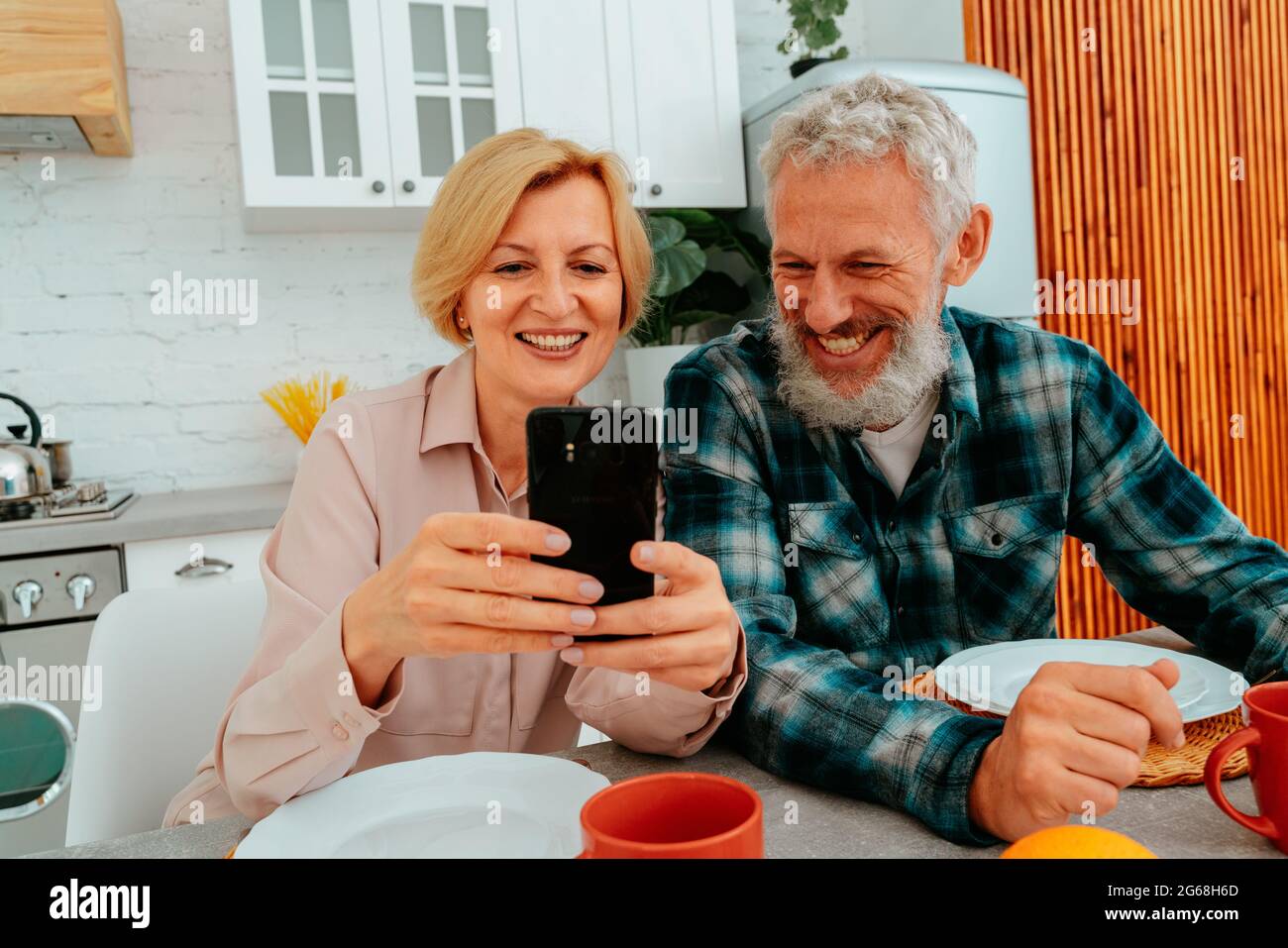 Das Paar frühstückt zu Hause und liest etwas vom Smartphone Stockfoto