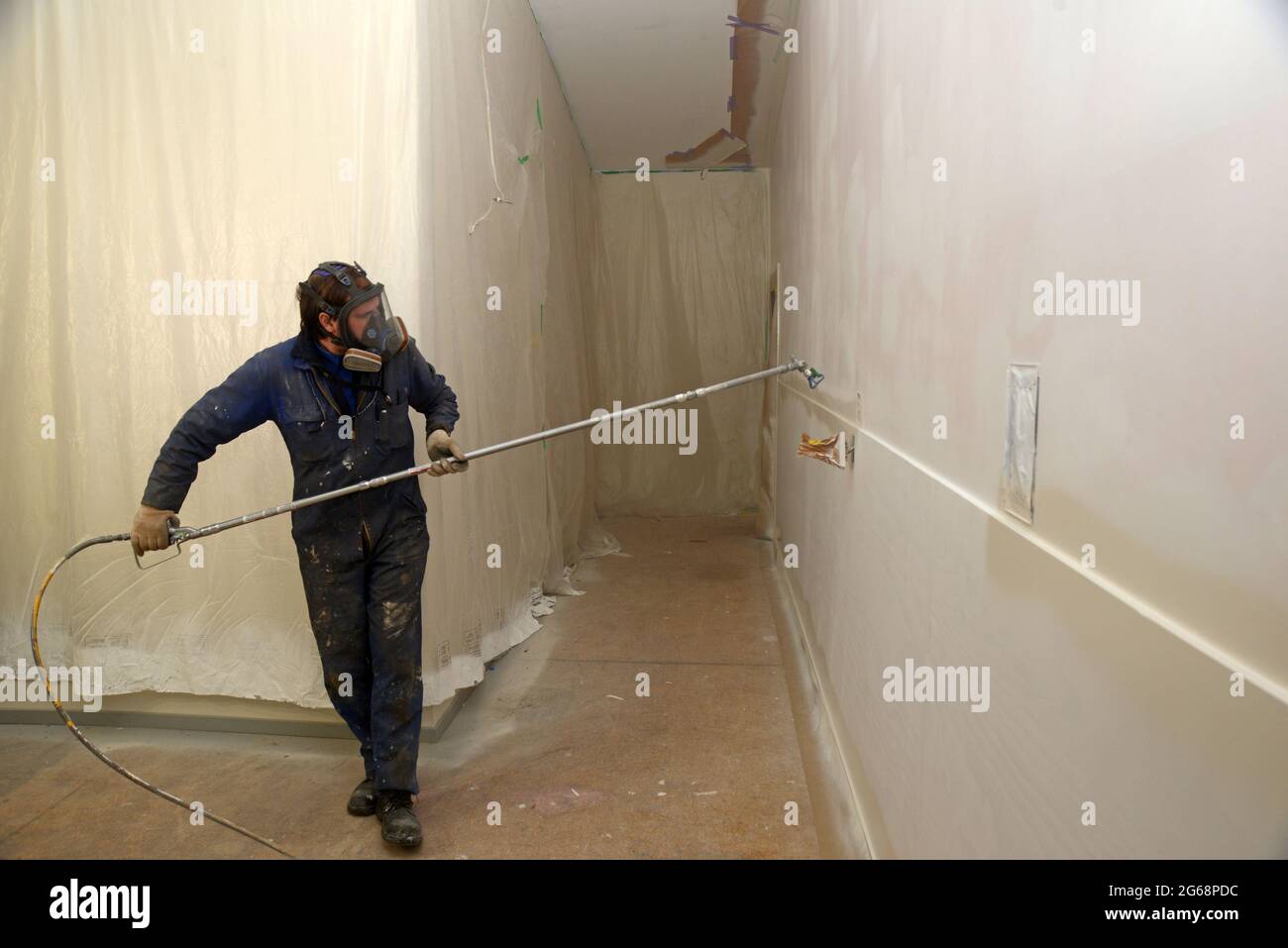 Ein Handwerker, der Airless-Sprühgeräte verwendet, um einen Decklack an die Wände eines Geschäftsgebäudes zu streichen Stockfoto