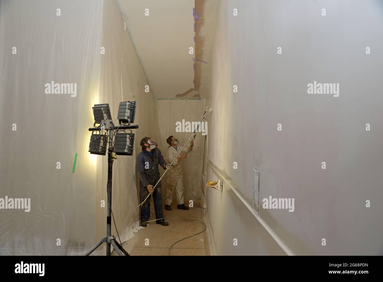 Zwei Handwerker verwenden Airless-Sprühgeräte, um einen Decklack auf die Wände eines Geschäftsgebäudes zu streichen Stockfoto
