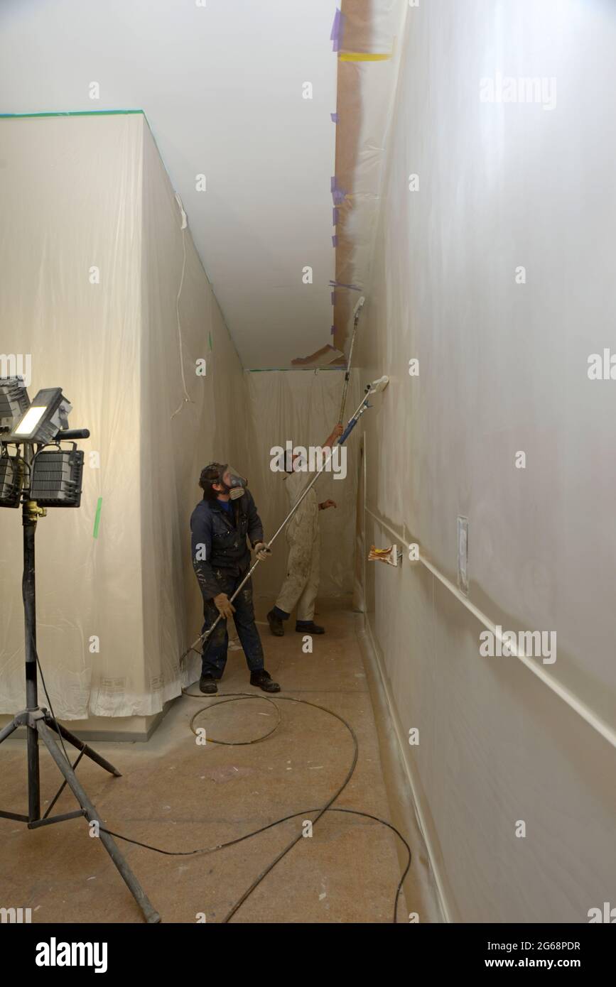 Zwei Handwerker verwenden Airless-Sprühgeräte, um einen Decklack auf die Wände eines Geschäftsgebäudes zu streichen Stockfoto