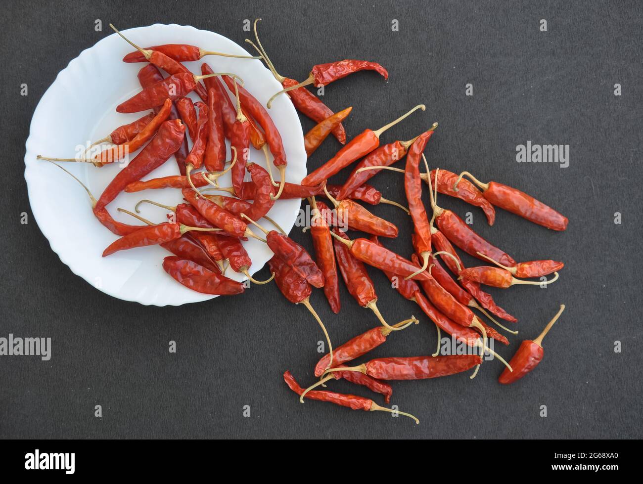 Haufen roter Chilischoten in weißer Platte mit Aufstrich auf rauer strukturierter schwarzer Farbtabelle mit negativem Abstand Stockfoto