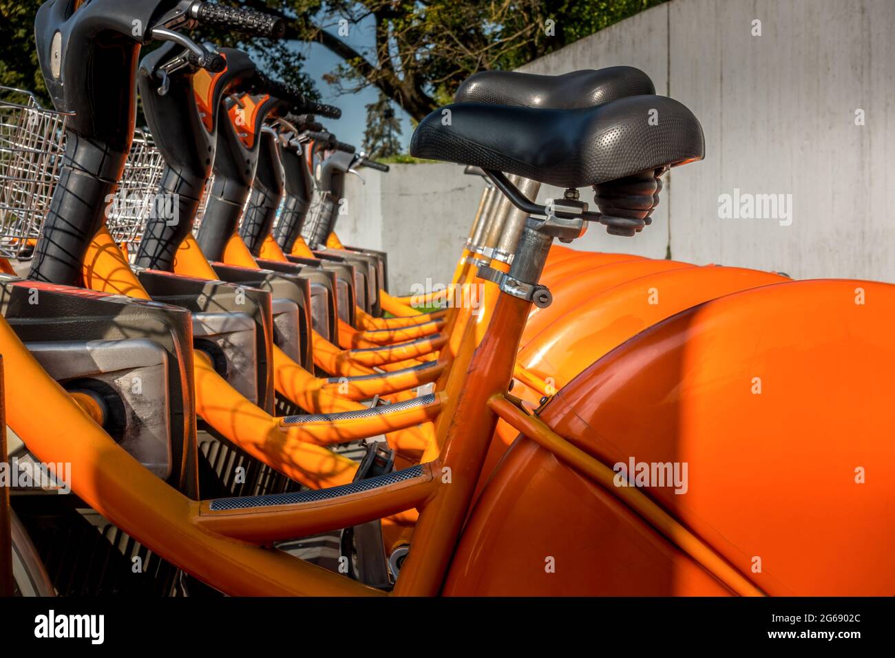 Orangefarbene Fahrräder standen auf dem Bürgersteig in der Stadt. Fahrradverkehr in der Stadt. Detail der Räder am Fahrradteilungspunkt. Moderner ökologischer Transport Stockfoto