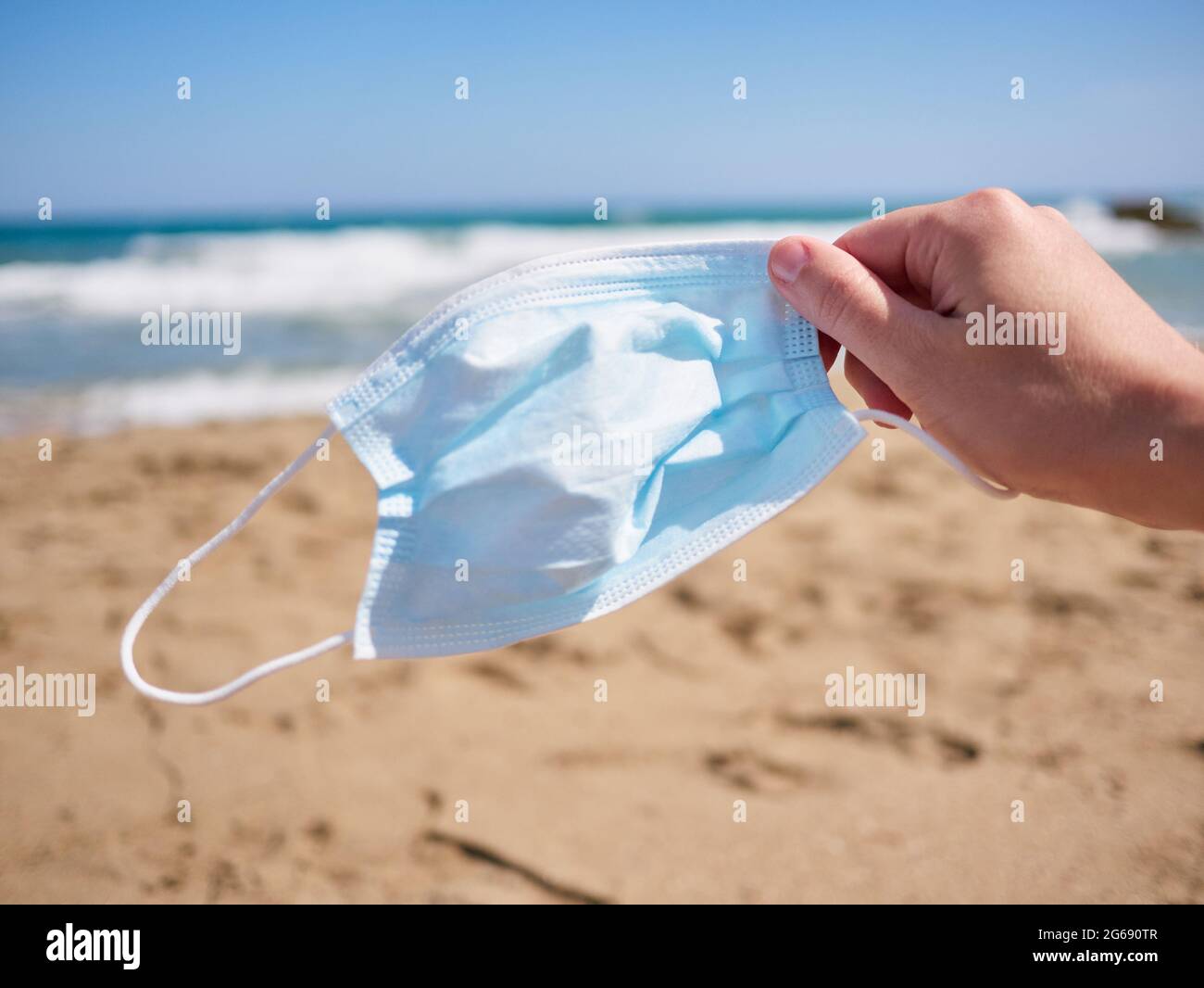 Hand hält eine Gesichtsmaske am Strand Stockfoto