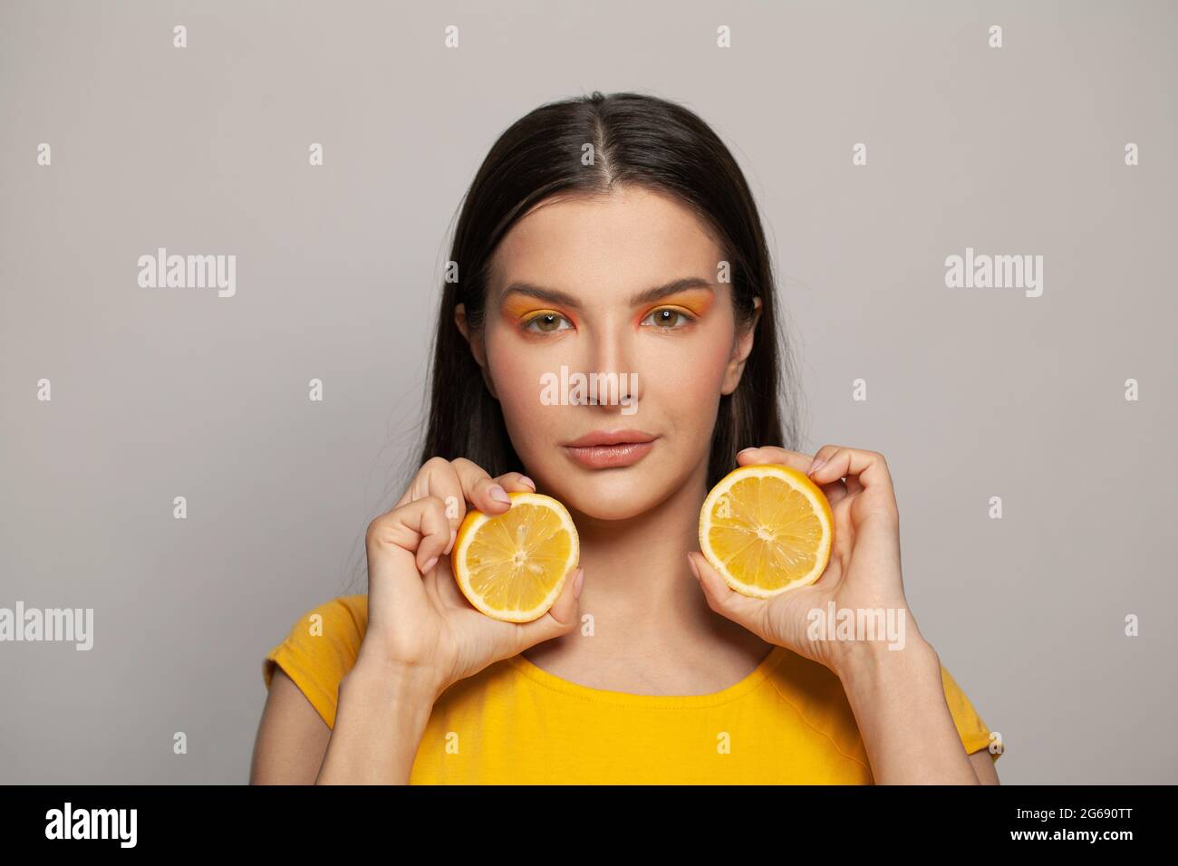 Perfekte junge Frau Brünette mit klarer Haut und geraden Frisur hält Zitronenfrüchte auf weißem Hintergrund. Diät, Hautpflege und Gesichtsbehandlung Konz Stockfoto