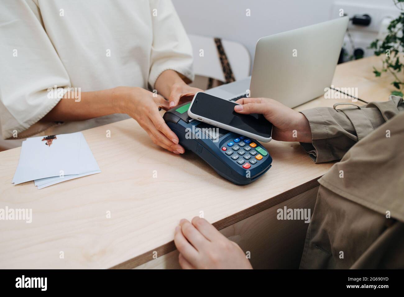 Frau, die mit ihrem Telefon an einem Geldautomaten bezahlt. Nur Hände. Verkäufer hält es mit beiden Händen. Stockfoto