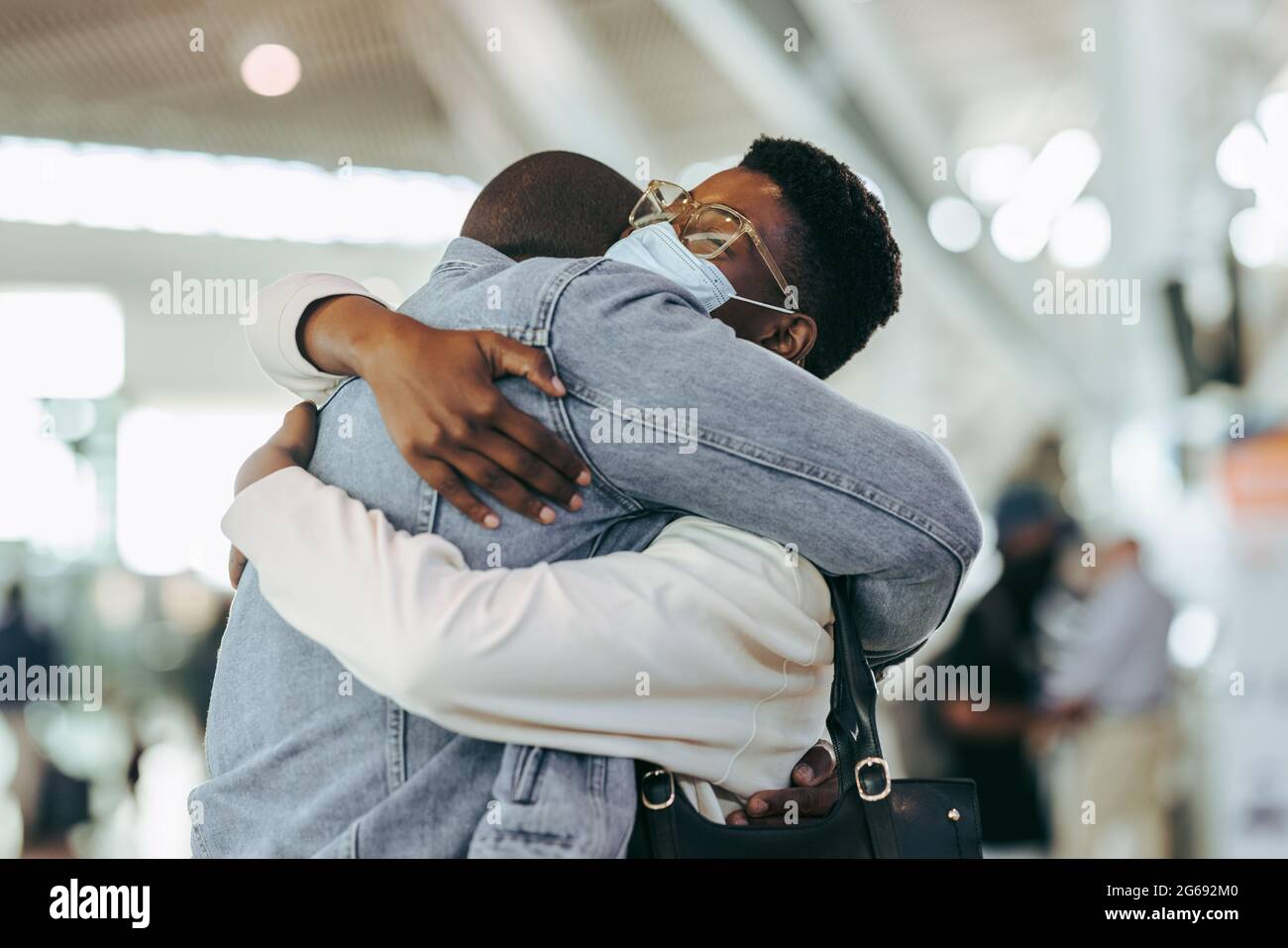 Mann umarmte Frau während einer Pandemie am Flughafenterminal. Afrikanisches Paar, das sich bei der Ankunft am Flughafen wiedervereinigt. Stockfoto